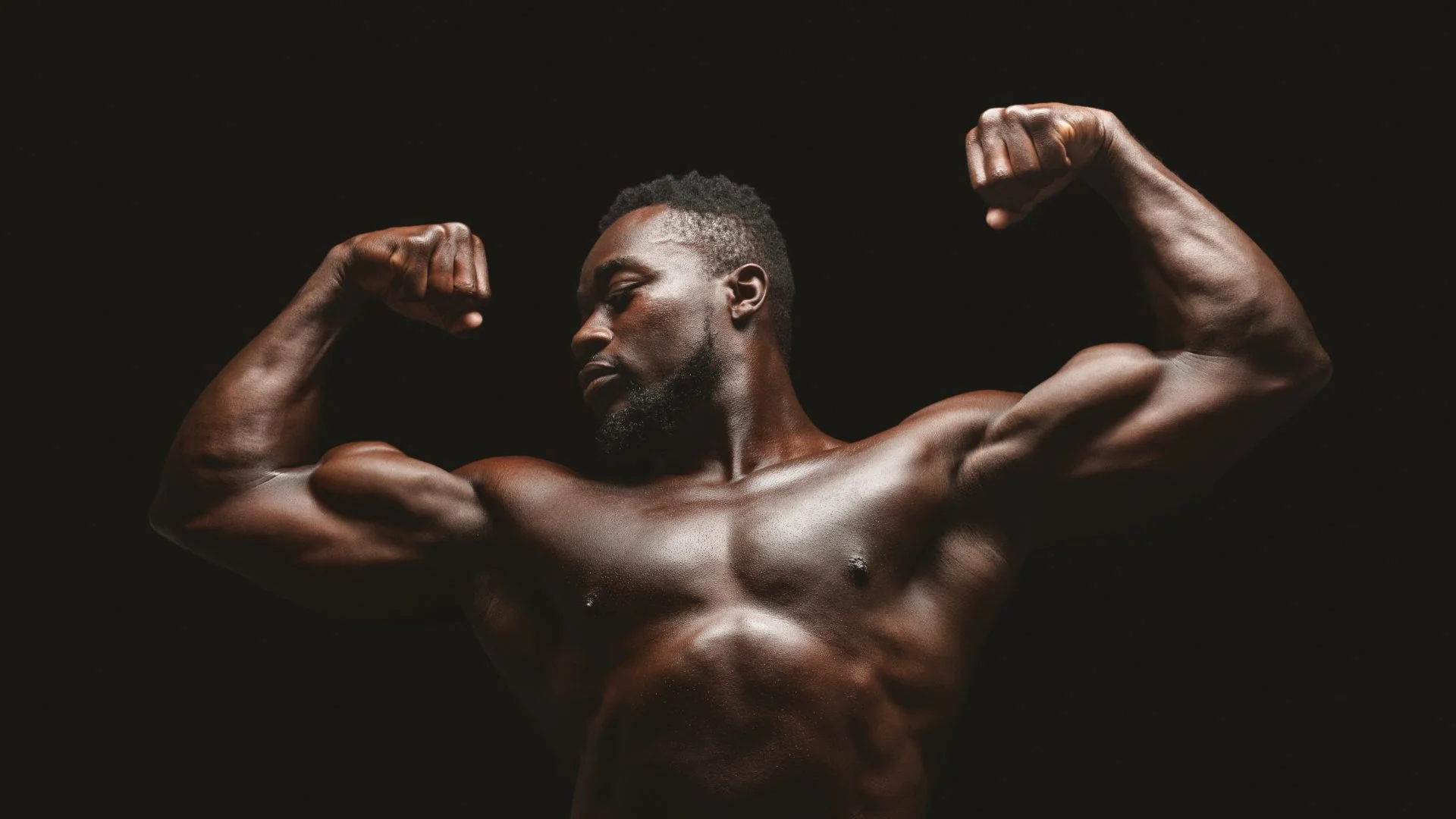 Athletic african fitness model flexing muscles over black studio background