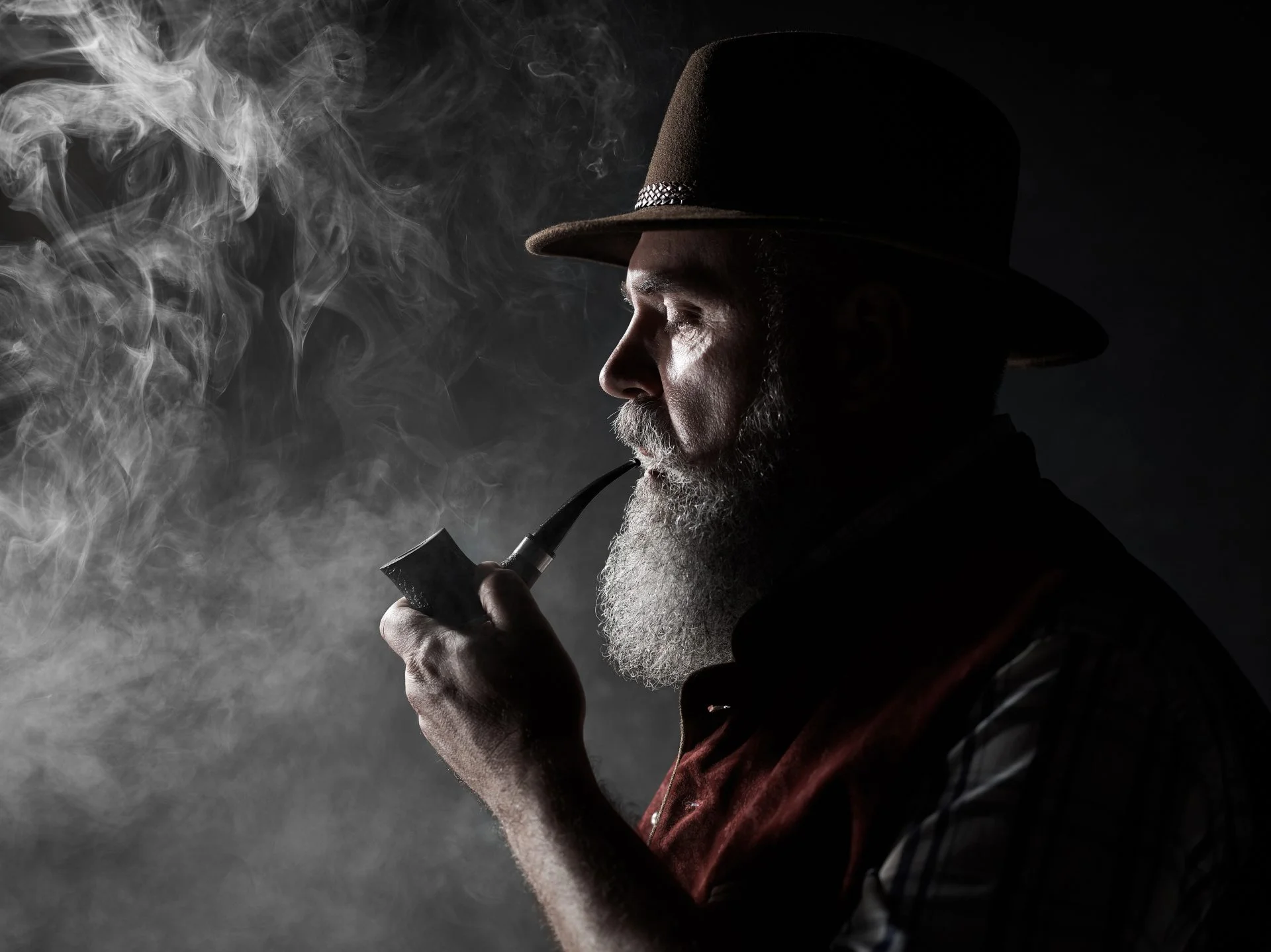 Black and white dramatic portrait of senior smoking tobacco pipe