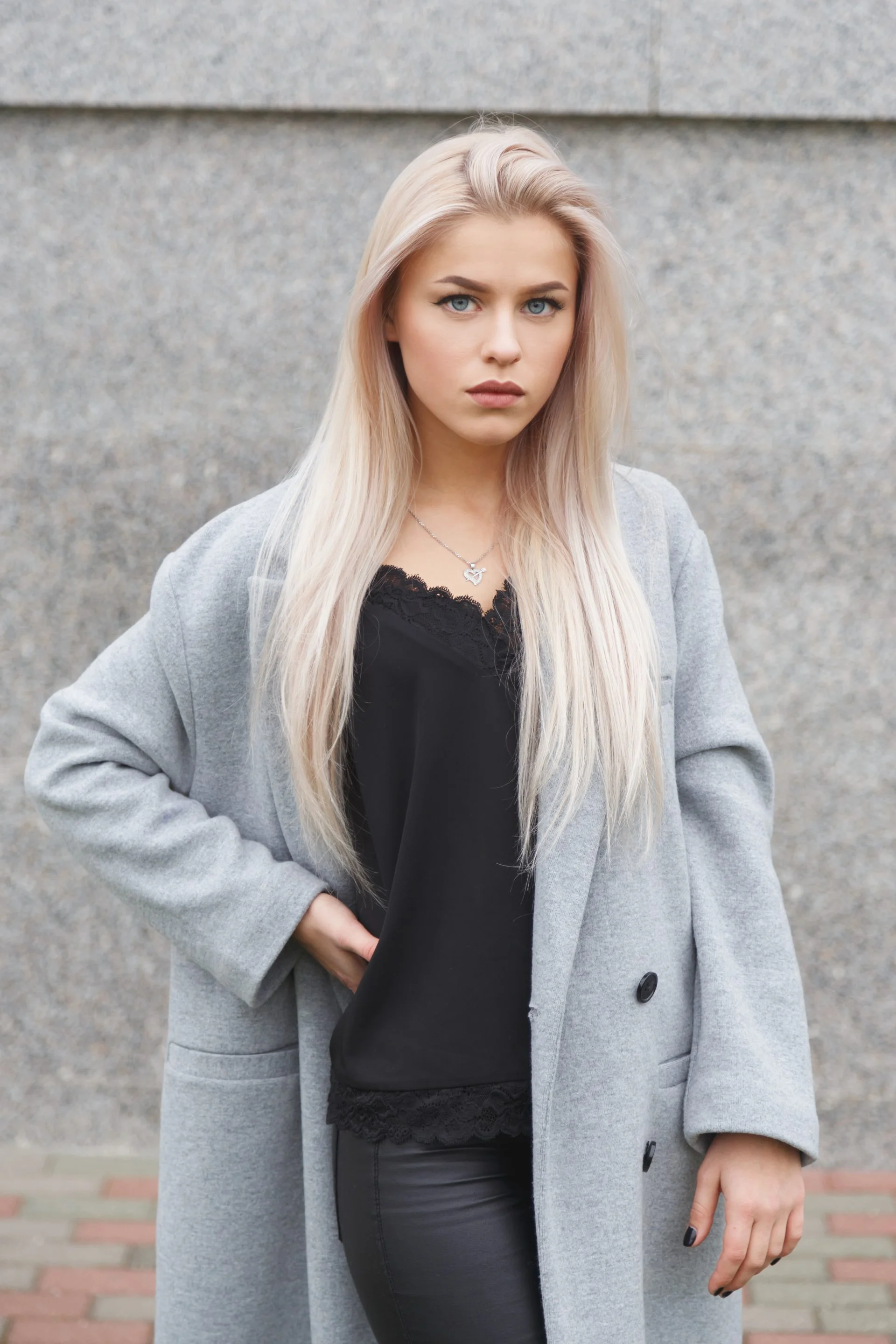 Portrait of a beautiful young blond woman in grey coat and black leather pants. Street fashion look