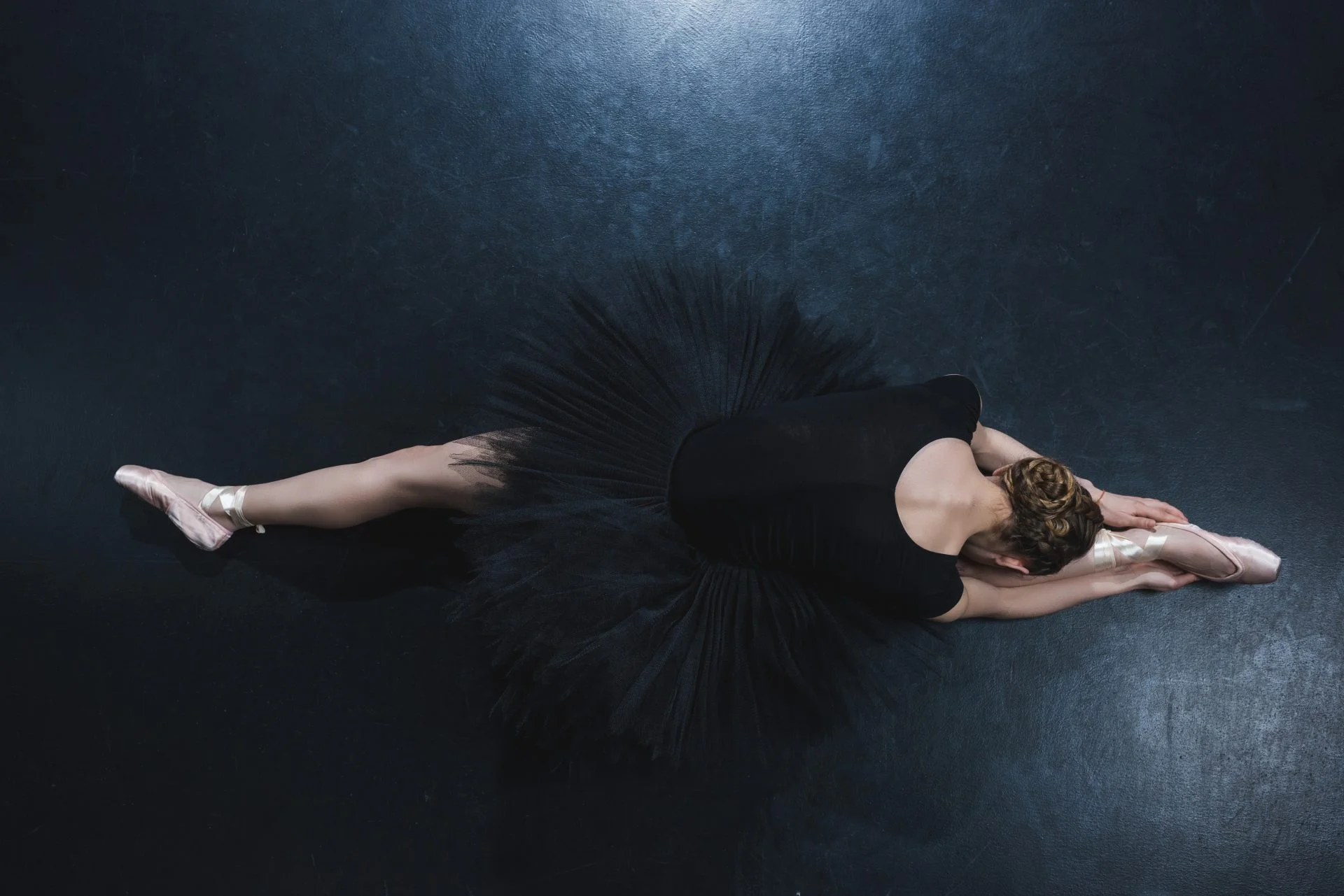 top view of elegant ballerina in pointe shoes and black tutu sitting on twine